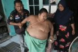 Rafka Adiputra (11) (tengah) penderita obesitas dibantu kedua orang tuanya saat akan beranjak dari tempat duduk di Desa Kedung Pengawas, Babelan, Kabupaten Bekasi, Jawa Barat, Kamis (10/3/2022). Rafka mengalami obesitas dari umur dua tahun dan saat ini berat badannya mencapai 115 kg. ANTARA FOTO/Fakhri Hermansyah/YU.