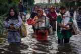 Sejumlah pedagang asongan pelabuhan berjalan menembus banjir limpasan air laut ke daratan atau rob yang merendam kawasan Pelabuhan Tanjung Emas Semarang, Jawa Tengah, Senin (23/5/2022). Banjir rob dengan ketinggian bervariasi hingga mencapai 1,5 meter itu disebabkan oleh tingginya pasang air laut serta adanya tanggul yang jebol di kawasan tersebut, sementara itu personel dari Basarnas, TNI-Polri dan relawan diterjunkan untuk membantu evakuasi para pekerja maupun warga. ANTARA FOTO/Aji Styawan/rwa.
