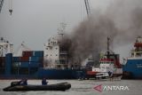 Kapal tunda (tug boat) memadamkan api yang membakar kapal kargo LIT Enterprise di Dermaga Jamrud Selatan, Pelabuhan Tanjung Perak, Surabaya, Jawa Timur, Kamis (13/10/2022). Sebanyak 15 kendaraan pemadam kebakaran dari Dinas Pemadam Kebakaran dan Penyelamatan Kota Surabaya serta PT Pelabuhan Indonesia (Persero) dikerahkan untuk memadamkan kebakaran kapal di pelabuhan itu. ANTARA Jatim/Didik Suhartono/zk