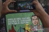 Warga memotret mural yang bertuliskan “Baru di era Jokowi belanja di Thailand bisa pakai rupiah” di Kabupaten Ciamis, Jawa Barat, Jumat (30/12/2022). Mural tersebut merupakan wujud ekspresi dari warga sebagai bentukan dukungan dan apresiasi terhadap kinerja pemerintah di era Presiden Joko Widodo. ANTARA FOTO/Adeng Bustomi/agr