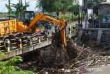 Petugas Badan Penanggulangan Bencana Daerah (BPBD) menggunakan alat berat mengangkat sampah yang menyangkut di tiang jembatan Sungai Piring Kota Madiun, Jawa Timur, Senin (13/2/2023). Pembersihan sampah yang terbawa air saat banjir dari darerah hulu dan menyangkut di pilar jembatan tersebut dimaksudkan untuk mitigasi bencana. ANTARA Jatim/Siswowidodo/zk