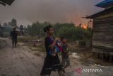 Kebakaran lahan di Kalsel mendekati permukiman warga. Seorang warga menggendong anaknya saat terjadi kebakaran lahan di dekat permukiman di Kecamatan Landasan ulin, Banjarbaru, Kalimantan Selatan, Jumat (23/6/2023). Kencangnya angin di lokasi kebakaran lahan membuat api dengan cepat menyebar yang diperkirakan mencapai puluhan hektare, dan hingga kini tim gabungan BPBD, Brimob dibantu relawan pemadam kebakaran masih berupaya memadamkan api yang mendekati permukiman penduduk di daerah setempat. ANTARA FOTO/Bayu Pratama S.