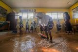 Pelajar dan guru membersihkan kelas yang terendam banjir di SDN 98 Kota Jambi, Jambi, Selasa (18/7/2023). Banjir yang terjadi akibat meluapnya anak sungai di belakang sekolah setelah kota itu dilanda hujan deras selama 3 jam lebih mengakibatkan hampir semua ruangan kelas terendam, dan selama tahun ini sekolah tersebut telah terdampak banjir hingga sepuluh kali. ANTARA FOTO/Wahdi Septiawan/aww.