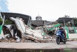 Warga melintas di dekat Masjid Jamik Al Muhajirin yang sebangian bangunannya roboh akibat gempa di Dusun Balikbakgunung, Sangkapura, Pulau Bawean, Gresik, Jawa Timur, Minggu (24/3/2024). Badan Penanggulangan Bencana Daerah (BPBD) Gresik mencatat sebanyak 4.085 rumah, 138 rumah ibadah, 68 sekolah, dan 12 perkantoran di Kecamatan Sangkapura dan Tambak mengalami kerusakan akibat gempa bumi yang berpusat di Kabupaten Tuban, Jawa Timur. ANTARA FOTO/Rizal Hanafi/Spt.