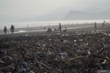 Sejumlah wisatawan melintas di dekat tumpukan sampah saat mengunjungi Pantai Bambang di Lumajang, Jawa Timur, Minggu (12/5/2024). Menurut warga setempat, sudah tiga pekan terakhir sampah yang terbawa banjir lahar hujan Gunung Semeru tersebut menumpuk di pesisir pantai itu.  Antara Jatim/Irfan Sumanjaya/um