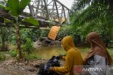 Warga mengamati kondisi Jembatan Sei Air Tenang yang ambruk di Padang Tualang, Langkat, Sumatera Utara, Kamis (20/6/2024). Jembatan penghubung  antara Kecamatan Padang Tualang dan Batang Serangan yang menjadi jalur menuju objek wisata Tangkahan tersebut ambruk setelah dilewati mobil damtruk bermuatan pasir dan batu yang melebihi muatan pada Selasa (11/6) lalu. ANTARA FOTO/Fransisco Carolio