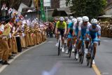 Sejumlah anak-anak memberikan semangat kepada pebalap dengan mengibarkan gambar bendera negara peserta pada Kejuaraan International Tour De Banyuwangi Ijen (ITDBI) 2024 di Banyuwangi, Jawa Timur, Rabu (24/7/2024). Pada etape ketiga ITDBI 2024 start dari Dusun Kakao Glenmore dan finish di depan Kantor Bupati Banyuwangi sejauh 166,8 kilometer tersebut Pebalap Ferei Quick-Panda Mongolia Team Nisu Oskar menjadi yang tercepat dengan waktu 3 jam 48.54 menit disusul pebalap Nusantara Arifin Muh Imam dan Pebalab Dr.J Cycling Team Novardianto Jamalidin. ANTARA Jatim/Budi Candra Setya/mas.