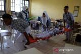 Dua pelajar  menggunakan tandu mengevakuasi temannya yang mengalami cidera patah kaki  saat berlangsung Simulasi Evakuasi Mandiri di Banda Aceh, Aceh, Rabu (9/10/2024). Simulasi Evakuasi Mandiri yang diawali di sekolah dan kemudian dilanjutkan evakuasi masal pelajar ke gedung penyelamatan Museum Tsunami Aceh itu dalam rangkaian Peringatan Bulan Pengurangan Resiko Bencana (PRB) dengan melibatkan sebanyak 3.565 pelajar SD, SMP dan SMA yang bertujuan meningkatkan kesiapsiagaan dan mengurangi resiko korban jika terjadi bencana. ANTARA FOTO/Ampelsa.