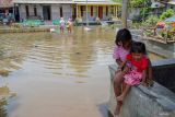 Dua anak duduk di atas teras yang tergenangan banjir akibat luapan sungai di Desa Rowokangkung, Lumajang, Jawa Timur, Jumat (22/11/2024). Pemerintah Kabupaten setempat telah berkoordinasi dengan pihak terkait untuk menormalisasi sedimentasi sungai sepanjang 1,5 kilometer penyebab banjir yang melanda 541 kepala keluarga di empat dusun sejak Rabu (20/11) agar warga bisa beraktivitas normal kembali. ANTARA Jatim/Irfan Sumanjaya/mas.