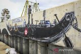 Warga melintas di atas tanggul laut bergambar mural bertema Balada Pesisir di tanggul laut Kampung Dadap, Kosambi, Kabupaten Tangerang, Banten, Minggu (15/12/2024). Pembuatan mural sepanjang 20 meter tersebut untuk menyampaikan aspirasi warga pesisir Kampung Dadap sekaligus mempercantik kawasan tanggul laut. ANTARA FOTO/Sulthony Hasanuddin/gp