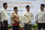 Menteri Koordinator Bidang Pemberdayaan Masyarakat (Menko PM), Muhaimin Iskandar (kedua kiri) menyerahkan bantuan dukungan pengembangan dapur dari Bank Syariah Indonesia sebesar Rp100 juta kepada Pengasuh Ponpes Mamba'ul Ma'arif KH Abdussalam Sohib (kedua kanan) disaksikan Kepala Badan Gizi Nasional, Dadan Hindayana (kanan) dan Deputi Bidang Koordinasi Pemberdaya Masyarakat Desa, Daerah Tertinggal dan Daerah Tertentu, Abdul Haris (kiri) saat uji coba kepada santri di aula Madrasah Aliyah Negeri (MAN) 4 Ponpes Mamba'ul Ma'arif Denanyar Jombang, Jawa Timur, Jumat (20/12/2024). Uji coba program makanan bergizi ini untuk mendukung program pemerintah di bawah kepemimpinan Presiden Prabowo Subianto serta sebagai persiapan sebelum pelaksanaan pemberian makan bergizi gratis secara resmi tahun pertama yang akan digulirkan mulai 6 Januari 2025 dengan anggaran Rp71 triliun untuk 17 juta orang, namun di tahun berikutnya akan ditambah hingga Rp400 triliun untuk mengcover semua wilayah di Indonesia. Antara Jatim/Syaiful Arif/um