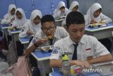 Siswa menyantap makanan bergizi gratis di SMP Negeri 2 Tasikmalaya, Kota Tasikmalaya, Jawa Barat, Senin (6/1/2025). Satuan Pelayanan Pemenuhan Gizi (SPPG) Tasikmalaya membagikan 2.999 paket makanan bergizi gratis kepada siswa di tujuh sekolah tingkat PAUD hingga SMA di Kota Tasikmalaya dengan menu makan berisi nasi, ayam goreng, tempe, tumis bucis dan wortel serta jeruk. ANTARA FOTO/Adeng Bustomi/agr