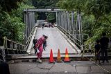 Warga melintasi Jembatan Cicangor yang ambles di Pangkalan, Karawang, Jawa Barat. Jembatan penghubung jalan provinsi yang menjadi akses utama dari Loji menuju Karawang kota atau sebaliknya itu amblas karena terkikis derasnya aliran sungai, akibatnya tidak bisa dilalui kendaraan roda empat maupun roda dua. ANTARA FOTO/Bayu Pratama S/rwa.