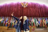 Sejumlah bendera negara peserta Konfrensi Asia Afrika (KAA) terpasang di belakang pengunjung yang berswafoto di ruang utama sidang Konfrensi Asia Afrika (KAA), Gedung Merdeka, Bandung, Jawa Barat, Rabu (16/4/2025). Konferensi Asia Afrika tahun ini menjadi peringatan ke-70 sejak pertama kali dilaksanakan pada 18 April 1955 yang diikuti 29 negara di Gedung Merdeka itu bertujuan sebagai solidaritas, persatuan serta menggelorakan semangat bagi negara-negara Asia dan Afrika dalam menyelesaikan masalah global. ANTARA FOTO/Novrian Arbi/agr