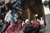 Peserta melintas di depan pengunjung yang sedang bermain gim melalui ponsel saat Pawai Kebaya di koridor kawasan pertokoan Kayutangan Heritage, Malang, Jawa Timur, Minggu (20/4/2025). Pawai dalam rangka memperingati Hari Kartini tersebut diikuti ratusan peserta dari berbagai komunitas penggemar kebaya maupun perajin batik. ANTARA Jatim/Ari Bowo Sucipto/mas.