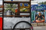 Pedagang bakso melintas di depan spanduk yang dipasang massa aksi di Gedung Sate, Jalan Diponegoro, Bandung, Jawa Barat, Selasa (22/4/2025). Aksi yang diselenggarakan dalam rangka Hari Bumi tersebut menuntut Pemerintah Provinsi Jawa Barat untuk mengevaluasi KSO seluruh tambang yang ada di Jawa Barat, realisasi kawasan Puncak Bogor-Cianjur sebagai nuansa etis bagi turis lokal serta berbagai permasalahan lingkungan yang belum terselesaikan di Jawa Barat. ANTARA FOTO/Raisan Al Farisi/agr