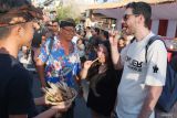 Wisatawan mancanegara mencicipi sate lilit khas Bali buatan siswa SMP pada Festival Semarapura ke-7 di Klungkung, Bali, Selasa (29/4/2025). Kegiatan yang diikuti puluhan siswa dari 12 sekolah tingkat SMP di wilayah tersebut digelar sebagai ajang edukasi serta mengenalkan siswa pada kekayaan kuliner tradisional khas Bali. ANTARA FOTO/Nyoman Hendra Wibowo/wsj.