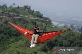 Wisatawan duduk di tempat tidur gantung (hammock) saat berwisata di Tebing Hawu, Padalarang, Kabupaten Bandung Barat, Jawa Barat, Senin (12/5/2025). Wisata ekstrem hammock di ketinggian sekitar 50 meter dari atas tanah dengan panorama perbukitan dan persawahan tersebut menjadi salah satu kegiatan wisata luar ruang favorit masyarakat untuk mengisi libur panjang Hari Raya Waisak 2025. ANTARA FOTO/Abdan Syakura/agr