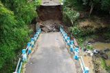 Foto udara warga berada di bawah jembatan yang ambrol di Desa Karangjati Anyar, Kecamatan Wonorejo, Pasuruan, Jawa Timur, Selasa (13/5/2025). Jembatan penghubung antarkecamatan tersebut ambrol disebabkan oleh dinding penahan yang tidak mampu menahan pergerakan tanah yang labil akibat intensitas hujan tinggi. Antara Jatim/Umarul Faruq