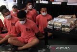 Sejumlah petugas kepolisian bersiaga di belakang beberapa tersangka yang dihadirkan dalam rilis ungkap kasus tindak pidana narkotika Polda Kalbar di Pontianak, Kalimantan Barat, Rabu (16/7/2025). Direktorat Reserse Narkoba Polda Kalbar merilis data pengungkapan 69 kasus tindak pidana narkoba periode Januari–awal Juli 2025, dengan jumlah tersangka 26 orang dan barang bukti berupa 23 kilogram sabu, 2.359 butir ekstasi, satu unit mobil, enam unit motor, serta sejumlah plat nomor palsu (plat merah dan plat hitam) yang ditemukan di dalam mobil salah satu tersangka. ANTARA FOTO/Jessica Wuysang