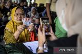 Petugas memotret warga memperlihatkan uang tunai saat penyaluran bantuan sosial di Kota Tangerang, Banten, Selasa (12/8/2025). Pemerintah Provinsi Banten telah menyalurkan bantuan sosial senilai Rp9,25 miliar kepada 18.500 keluarga penerima manfaat (KPM) dari total anggaran Rp18,8 miliar untuk 37.741 KPM pada tahun 2025. ANTARA FOTO/Putra M. Akbar/gp