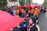 Sejumlah peserta mengarak kain warna merah dan putih raksasa di Kota Kediri, Jawa Timur, Sabtu (16/8/2025). Kain yang terbagi dalam delapan potongan tersebut akan disatukan menjadi bendera merah putih raksasa selebar 40 meter x 60 meter dan akan dikibarkan pada tanggal 17 Agustus di atas pegunungan Klotok guna memperingati HUT ke-80 kemerdekaan RI. Antara Jatim/Prasetia Fauzani/um