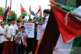 Pengunjuk rasa yang tergabung dalam Masyarakat Aceh Peduli Palestina membawa bendera dan poster menggelar  aksi solidaritas di Banda Aceh, Aceh, Minggu (12/10/2025). Aksi Masyarakat Aceh Peduli  Palestina itu  meminta peran aktif Pemerintah Indonesia  mengawal gencatan senjata antara Palestina dengan Israel dan menolak  Genosida. ANTARA FOTO/Ampelsa.
