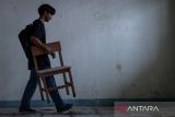 Siswa mengangkat kursi di samping coretan pada dinding kelas di SMK Al-Anshor, Legok, Kabupaten Tangerang, Banten, Selasa (21/10/2025). Menurut keterangan siswa, sekolah tersebut menghentikan kegiatan belajar mengajar tatap muka sejak Agustus 2025 dengan kondisi sarana dan prasarana yang rusak serta jumlah siswa aktif tersisa sebanyak 26 orang dan empat guru yang hingga kini masih menanti kejelasan terkait kelanjutan masa depan pendidikannya. ANTARA FOTO/Putra M. AkbarA/gp