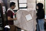 Pengusaha batik generasi Z, Satrya Paramanandana (kiri) melakukan kontrol kualitas kain batik tulis yang diproduksi pekerjanya di Galeri Batik Soendari, Malang, Jawa Timur, Selasa (28/10/2025). Pengusaha berusia 25 tahun tersebut memberdayakan puluhan warga sekitar untuk memproduksi 50 hingga 100 lembar batik per bulan yang dipasarkan ke berbagai kota di Indonesia serta diekspor ke Filipina, Malaysia, dan China dengan harga antara Rp50 ribu hingga Rp6 juta per lembar, bergantung pada tingkat kerumitan motifnya. ANTARA Jatim/Ari Bowo Sucipto/mas.