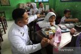 Kepala Satuan Pelayanan Pemenuhan Gizi (SPPG) Polrestabes Medan Adi Teguh Santoso (kiri) menyaksikan siswa menyantap makanan bergizi gratis saat   pelaksanaan program Makan Bergizi Gratis di SDN 106162 Percut Sei Tuan, Kabupaten Deli Serdang,  Sumatera Utara,  Selasa (4/11/2025). SPPG Polrestabes Medan mendistribusikan sebanyak 3.960 porsi makan bergizi gratis untuk siswa SD di 14 sekolah serta balita, ibu hamil dan ibu menyusui.ANTARA/Yudi Manar