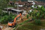 Petugas Badan Penanggulangan Bencana Daerah (BPBD) dengan menggunakan alat berat menyingkiirkan reruntuhan material yang menimbun jalan akibat longsor di Desa Wagir Kidul, Pulung, Ponorogo, Jawa Timur, Kamis (20/11/2025). Petugas BPBD bersama warga menyingkirkan reruntuhan material dan pembenahan rumah yang rusak dan tertimbun pascabencana tebing longsor yang mengakibatkan dua rumah warga rusak dan tertimbun, tiga unit mobil dan empat sepeda motor serta jalan tertimbun, Rabu (19/11). Antara Jatim/Siswowidodo/um