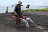Wisatawan mancanegara menyaksikan petani menyiram air laut ke lahan pasir saat pembuatan garam tradisional di Klungkung, Bali, Rabu (3/12/2025). Menurut petani setempat, jumlah kunjungan wisatawan mancanegara ke rumah produksi garam tradisional tersebut rata-rata 5-10 orang per hari untuk melihat proses pembuatan garam sekaligus membeli garam yang dijual seharga Rp20 ribu-Rp40 ribu per bungkus sesuai ukuran. ANTARA FOTO/Nyoman Hendra Wibowo/wsj.