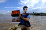 Seorang relawan mengenakan topeng sambil memperlihatkan poster berisi seruan penyelamatan lingkungan saat menggelar aksi di Sungai Kapuas, Pontianak, Kalimantan Barat, Rabu (3/12/2025). Dalam aksi yang digelar para relawan dari Greenpeace, Tim Cegah Api, Gemawan, GMNI Kalbar, dan Extinction Rebellion Pontianak untuk memperingati Hari Relawan Sedunia tersebut mereka menyuarakan sejumlah isu, antara lain selamatkan bumi, penghentian pembakaran hutan dan lahan, pukul mundur krisis iklim, serta penyelamatan hutan dan ekosistem gambut. ANTARA FOTO/Jessica Wuysang
