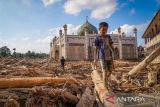 Seorang bocah berjalan meniti kayu-kayu yang memenuhi area Pondok Pesantren Darul Mukhlishin pascabanjir bandang di Desa Tanjung Karang, Karang Baru, Kabupaten Aceh Tamiang, Aceh, Jumat (5/12/2025). Usai sepekan setelah bencana banjir bandang, akses menuju Desa Tanjung Karang masih terhambat akibat banyaknya tumpukan pohon dan lumpur tebal dari Sungai Tamiang sehingga bantuan sulit masuk ke wilayah tersebut. ANTARA FOTO/Erlangga Bregas Prakoso/rwa.