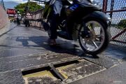 Pengendara roda dua melintas dekat plat besi jembatan gantung