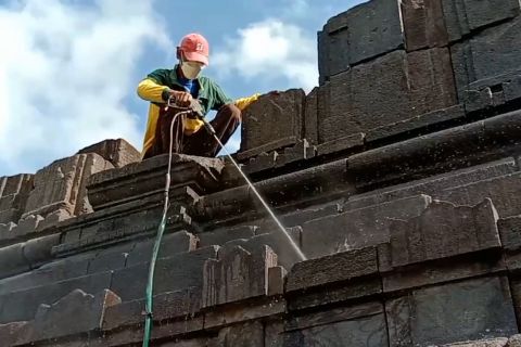 Petugas semprotkan air besihkan abu Merapi di Candi Asu
