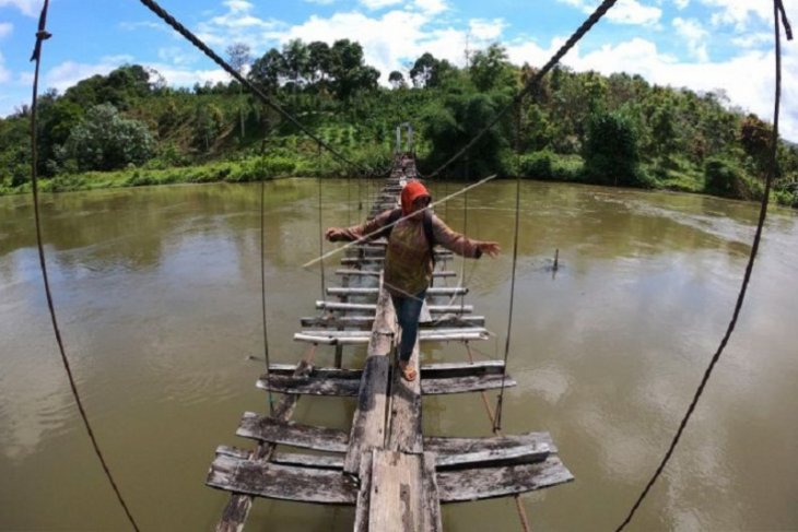 Seorang wanita menyeberang di atas jembatan rusak di Kerinci