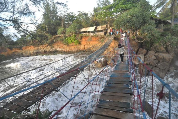 Pengunjung menyeberangi Jembatan Cinta di kawasan objek wisata Pantai Sungai Suci